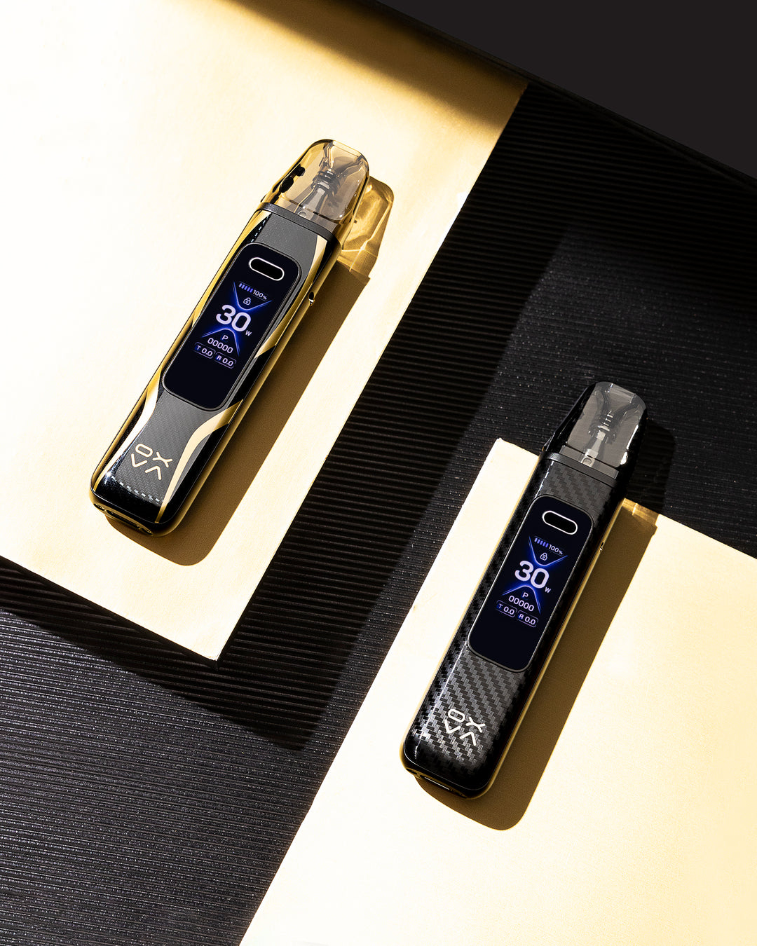 Two oxva vaping devices with digital displays on a black and gold background